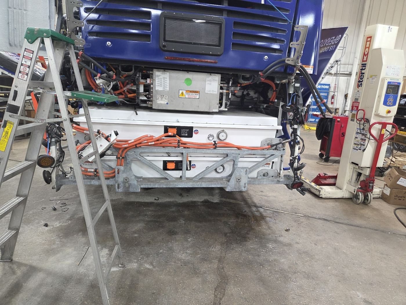 Front of a transit bus opened up on a lift for high voltage system work