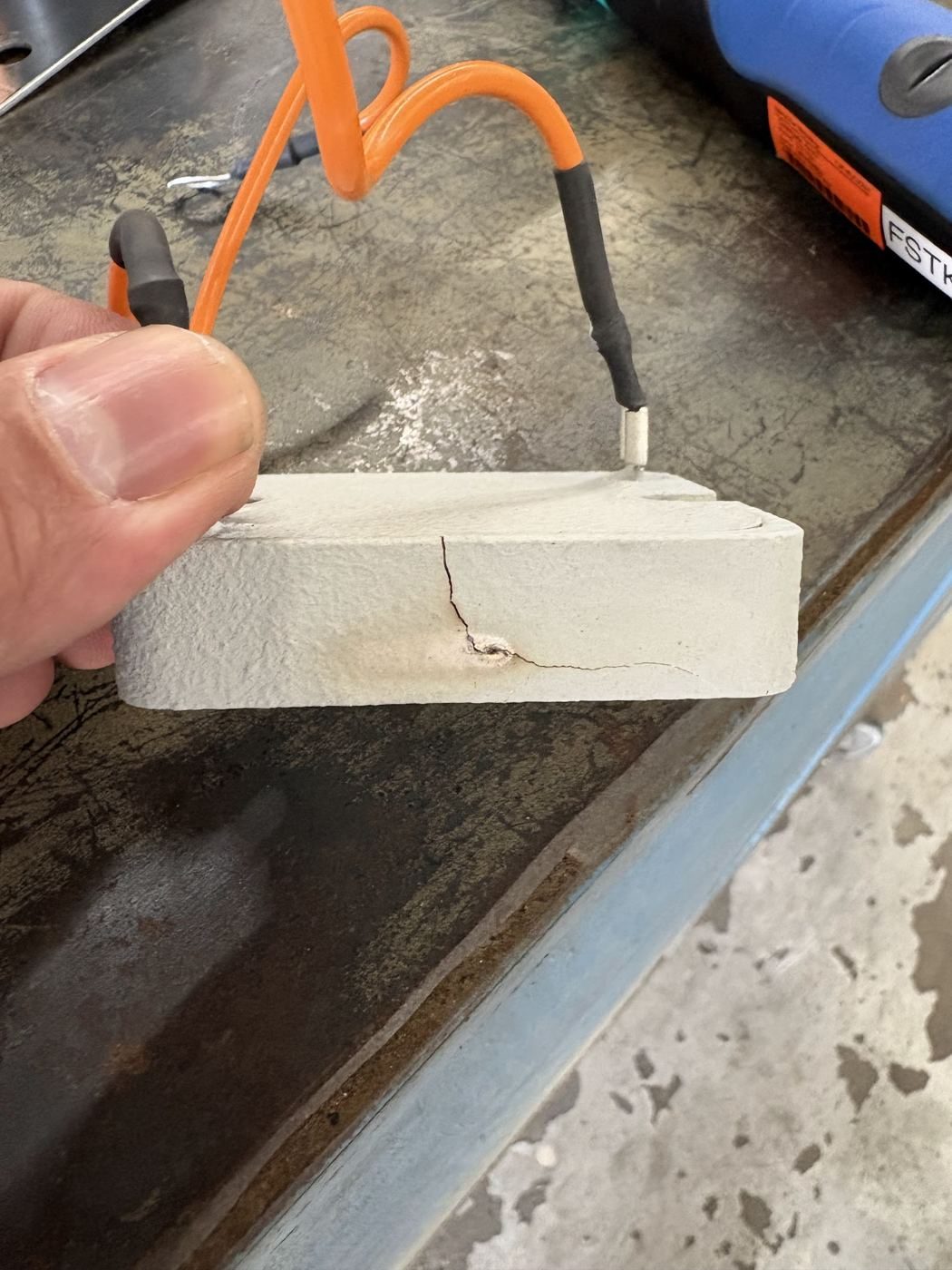 Hand holding a cracked, overheated ceramic pre-charge resistor removed from a battery pack